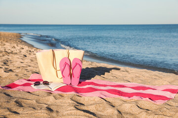 Towel with book and beach accessories on sand near sea, space for text