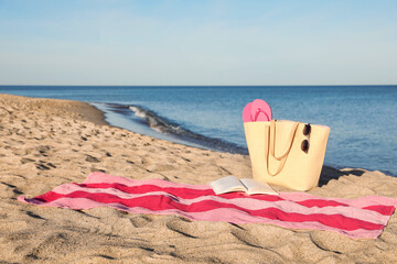 Towel with book and beach accessories on sand near sea, space for text
