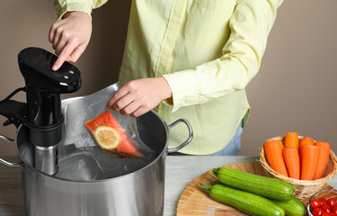 Woman putting vacuum packed salmon into pot and using thermal immersion circulator at table,...