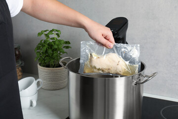 Woman taking out vacuum packed meat from pot in kitchen, closeup. Thermal immersion circulator for...