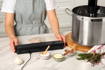 Woman using sealer for vacuum packing in kitchen, closeup. Sous vide cooking