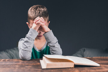 Holy Bible on the table. A boy prays with folded hands in prayer. Pray to God
