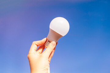 Energy-saving lamp in hand against a clear gradient blue sky. The concept of ecology, environmental conservation and a new idea.