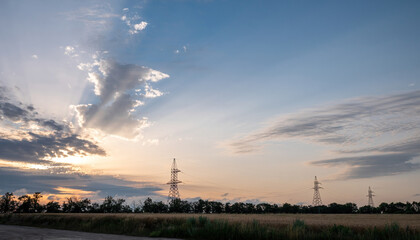 Power transmission lines transfer clean energy. Sunset illuminates countryside farmland with power...