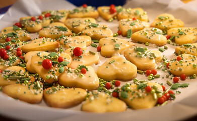 closeup view over a tray of fresh baked homemade christmas cookies, shape of hearts, decorated with sugar coating and colorful sugar beads, backlight, blurred background