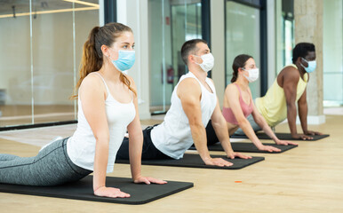 Obraz premium Multiethnic group of young adult people in protective face masks practicing pilates together at fitness center during coronavirus pandemic