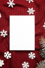 Christmas greeting card mockup, fir tree branches and holiday decorations on red knitted sweater background, top view, flat lay. Blank New Year card with winter decor, white wooden snowflakes
