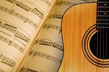 The fretboard of an old vintage acoustic guitar with strings next to sheets of music. A musical...