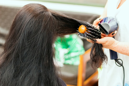 A stylist combing a woman's long black hair using a hair dryer and a roller brush