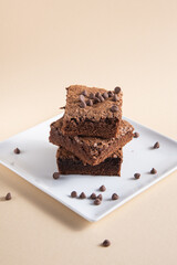 tower of three brownies with chocolate chips on a square white dish with a beige background