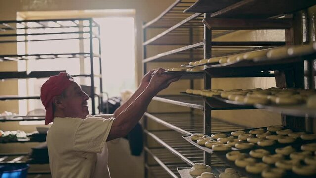 Hombre colocando panes y galletas en el estante para ser horneados.  Concepto de panadería y pastelería.