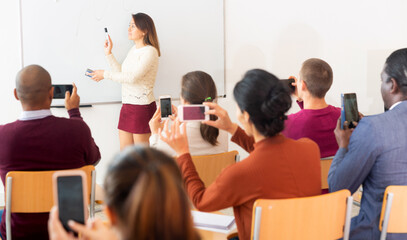 Obraz premium .Female teacher standing in front of whiteboard and people shooting on smartphones her