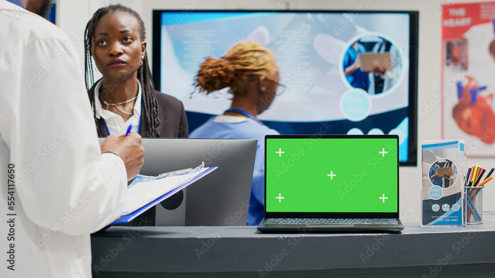 Poster people working with greenscreen display on laptop in facility lobby, using checkup form papers in he