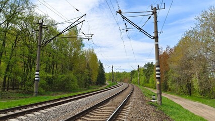 Railway rails are laid on concrete sleepers and sprinkled with crushed stone. The railroad is electrified, along the rails installed concrete poles with wires. Near there are grassy lawns and trees 