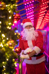 Fototapeta na wymiar Portrait von einem verkleideten Weihnachtsmann, der auf einem Weihnachtsmarkt von bunten Lichtern umgeben ist