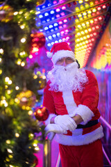 Fototapeta na wymiar Portrait von einem verkleideten Weihnachtsmann, der auf einem Weihnachtsmarkt von bunten Lichtern umgeben ist