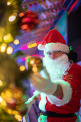 Portrait von einem verkleideten Weihnachtsmann, der auf einem Weihnachtsmarkt von Bokeh von bunten Lichtern umgeben ist