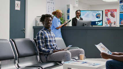 African american man waiting to attend consultation with medic, sitting in hospital reception. Young adult in waiting area having exam appointment with specialist to cure disease at health center.