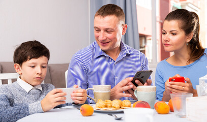 Parents and teen son using phones at kitchen. High quality photo