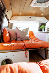 Young 30s caucasian woman with dark hair making the bed in a self converted minivan campervan for...