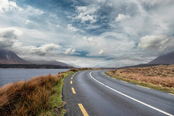 Beautiful scenery and small road by a lake in Connemara, Ireland. Mountains and cloudy sky in the...