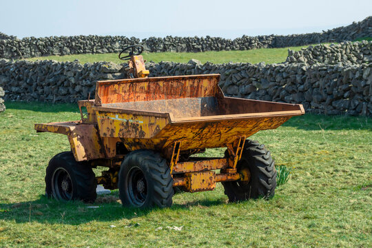 Small old rusty mini dumper truck in a green field. Stone wall in the background. Agriculture and farming industry, West of Ireland.