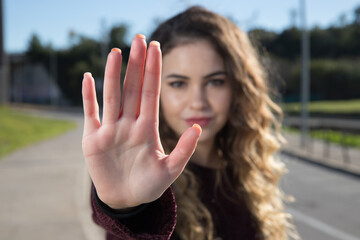 Close up focus on woman showing stop gesture at camera, blurred background, strong young female...