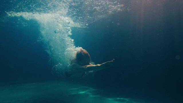 Woman dives in the pool. Underwater view of the girl diving in the pool and gliding underwater with bubbles