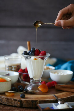 Fruit and yogurt parfait with dripping honey on wood background