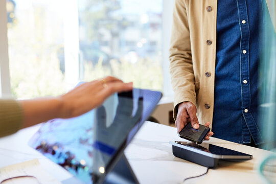 Male customer taping smart phone on POS system in coffee shop