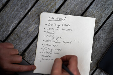 gril writing a camping list in a piece of paper. writing a check list with a pencil