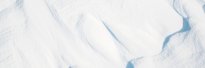 Obraz premium Wide panoramic winter background with snowy ground. Natural snow texture. Wind sculpted patterns on snow surface.