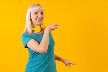 Pointing ads to the right with headphones, blonde caucasian girl on yellow background studio