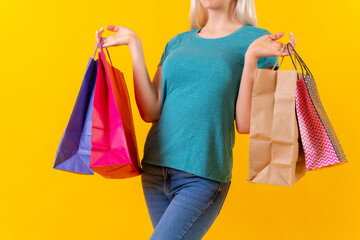 Unrecognizable person with colored shopping bags on sale, yellow background studio