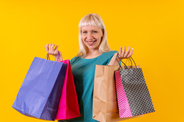 smiling shopping with bags on sale, blonde caucasian girl in studio on yellow background