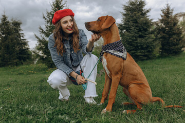 Happy woman caressing obedient Rhodesian Ridgeback puppy on leash on green meadow in park in summer 