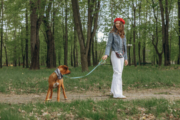 Full length of content female owner standing with brown Rhodesian Ridgeback dog on leash during...