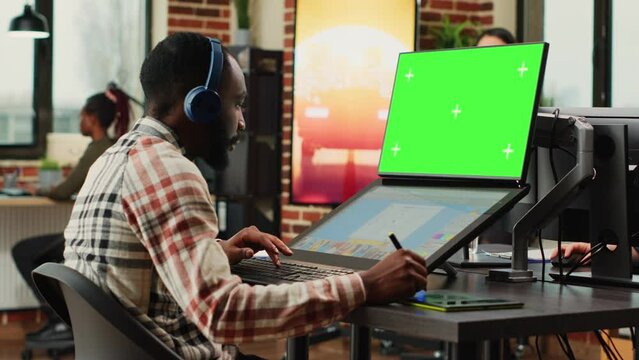 Young content creator using greenscreen background on computer, retouching photos with editing software. Male employee working with isolated chroma key display and blank copyspace.