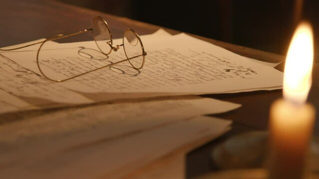 Candlelit scene from the 1800s of eyeglasses lying on an open letter written with a dip pen of the era.