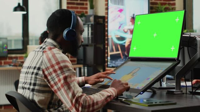 African american editor using greenscreen template on monitor, retouching photos with editing software. Male employee working with isolated chroma key display and blank copyspace.