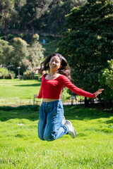 Fototapeta premium young woman jumping happily looking at the camera against a nature background