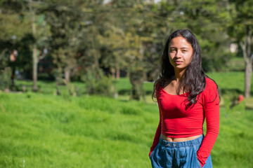 Obraz premium young woman smiling looking at the camera with a red jacket on the side with a nature and forest background