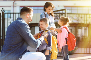 Young parents saying goodbye to their little children near school