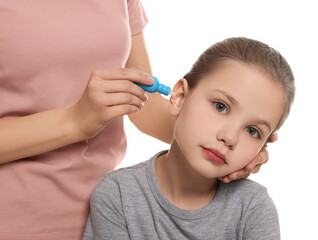 Mother dripping medication into daughter's ear on white background