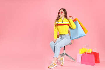 Fototapeta na wymiar Happy woman in stylish sunglasses holding many colorful shopping bags on armchair against pink background