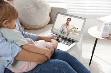 Mother and daughter having online consultation with pediatrician via laptop on sofa at home