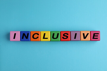 Colorful cubes with word Inclusive on light blue background, flat lay