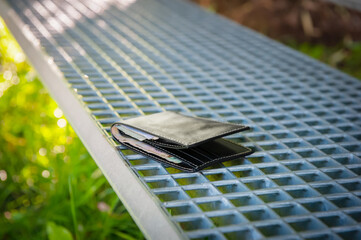 Black wallet on metal bench outdoors. Lost and found