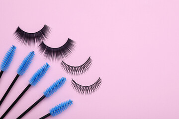 Fake eyelashes and brushes on pink background, flat lay. Space for text