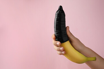 Woman holding banana in condom on pink background, closeup and space for text. Safe sex concept